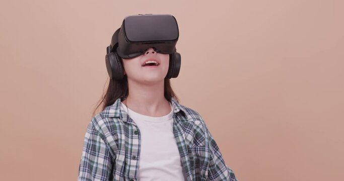 A girl having fun with game while wearing virtual reality glasses. Isolated on brown background in studio.