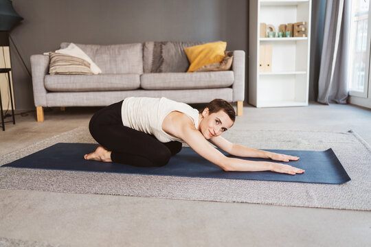 Active 30-Year-Old Woman with Short Hair Stretching After Workout in Her Cozy Living Room, Smiling at the Camera.