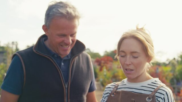 Close up of woman wearing apron and mature man working outdoors in garden centre holding digital tablet - shot in slow motion