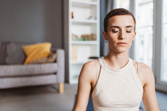 Serene 30-Year-Old Woman with Short Hair Practicing Yoga with Closed Eyes in Modern Living Room