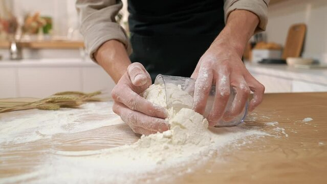 A cook in the kitchen sifts flour through a sieve. Kneading raw dough with male hands. Breaks an egg. White flour.	