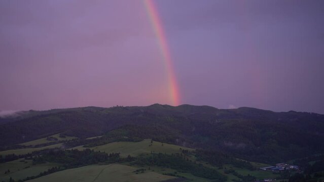 Drone shot of the rainbow in the cloudy dusk sky over a green dense woods after a storm in Slovakia