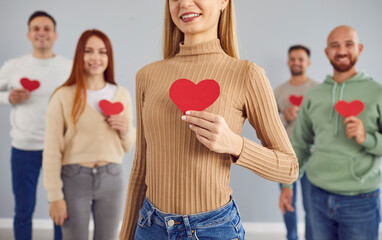 Group of diverse volunteer people comes together, holding a red heart. Smiles radiate happiness,...