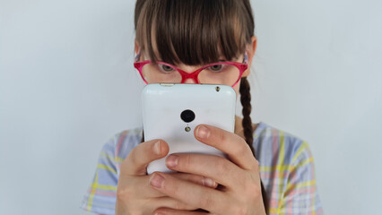 Portrait of a serious little girl with poor eyesight sending text messages on social networks on...