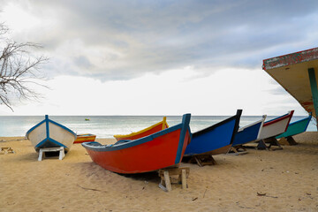 Cluster of fishing boats resting on the sandy shoreline near a destroyed building.
