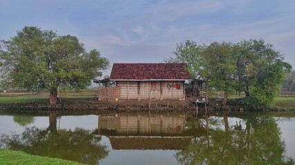 An old wooden house made from woven bamboo next to the fish pool in village area