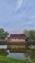 An old wooden house made from woven bamboo next to the fish pool in village area
