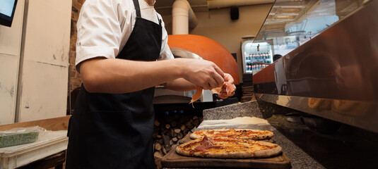 In the busy kitchen of a pizzeria, a chef skillfully tops a baked pizza with delicate slices of...