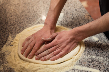 Close-up on the hands of a chef stretching pizza dough on a floured surface, the start of an authentic pizza-making process