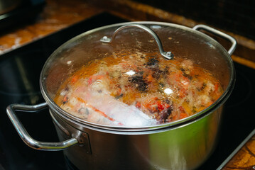 Homemade Soup Cooking in Large Pot. A large pot of homemade soup simmering on the stove with a mix of vegetables and meats, steaming under a closed lid.