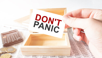 Businessman hold white card with text DON'T PANIC Calculator, wood box, money and financial...