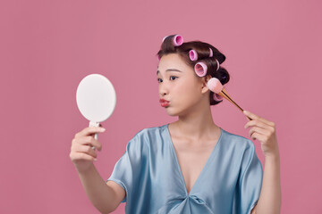 Pretty woman with curlers on hair, holding makeup brushes and mirror in hands