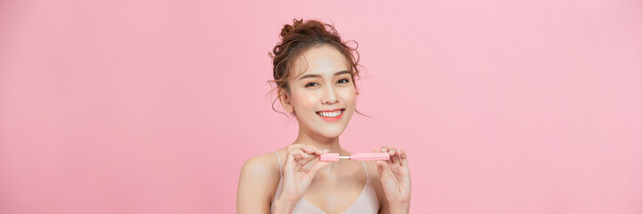 Young woman using lip gloss looking at camera on pink studio background