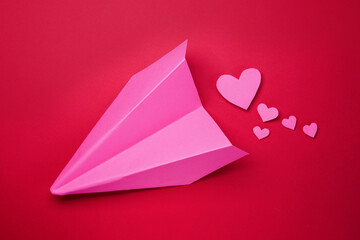 Creative composition with pink paper plane and hearts on a red background. Valentines Day celebration. Flat lay, top view. 
