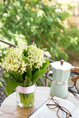 Composition with spring flowers lily of the valley, book and glasseson it and coffee pot on table....