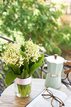 Fototapeta Composition with spring flowers lily of the valley, book and glasseson it and coffee pot on table. Good morning concept. Side view.