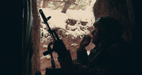 An elderly soldier sits with a machine gun in a trench, dugout and smokes. Military actions in the...