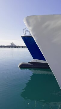 A moored ship rocks on the waves. Reflection in the water of the port at the pier. Ropes hold the white ship at the pier. Spain. Grao, Castellon