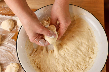 A woman forms pieces of dough for making donuts. The process of making donuts