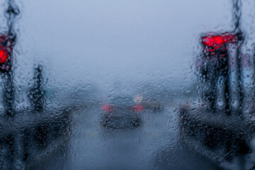 Water droplets on a car windshield during monsoons with red signals and car taillights in the out...