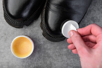 Female's hands taking care of leather shoes on gray background.