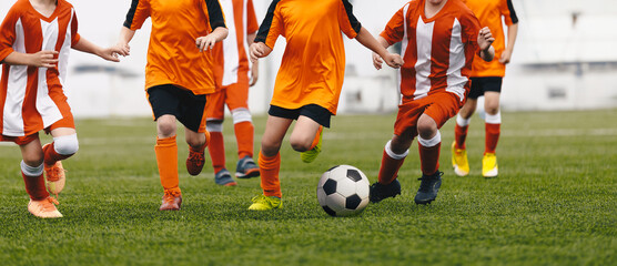 Cchildren having fun in soccer football game. Group of school kids running ball in football duel. School boys in sports outdoor competition. Children in red and orange soccer uniforms - Powered by Adobe