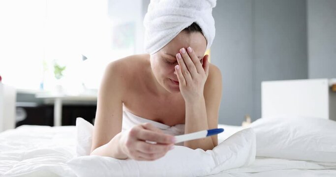 Upset woman holding pregnancy test and crying on bed. Unplanned pregnancy and stress concept