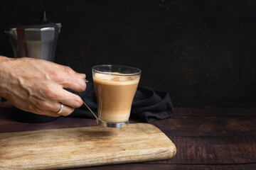 Man's hand holding cup of coffee with milk on wooden table and Italian coffee pot