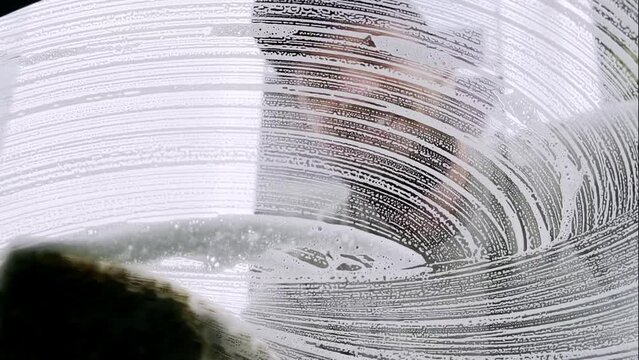 happy man washing car window using sponge and window cleaning foam, home car washing concept. High quality 4k footage