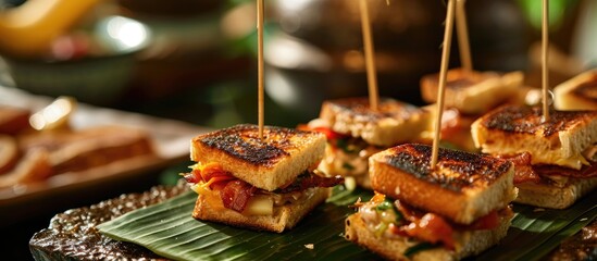 Restaurant service featuring bite-sized grilled cheese and bacon sandwiches on bamboo toothpicks and banana leaf garnish. - obrazy, fototapety, plakaty
