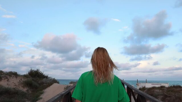 blonde girl in a green Tshirt goes to the beach. the girl turns her back to the camera. High quality FullHD footage