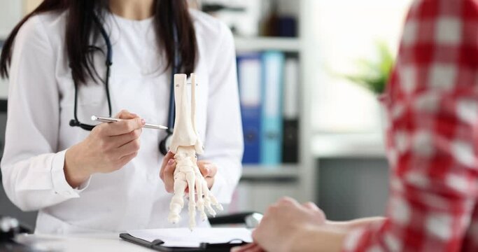 Doctor traumatologist shows model of a plastic leg of person to patient with problem with feet. Foot anatomy and skeleton concept