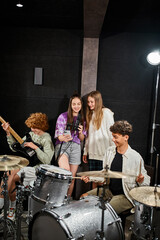 cheerful teenage girls singing while boys playing their drums and guitar in studio, musical group