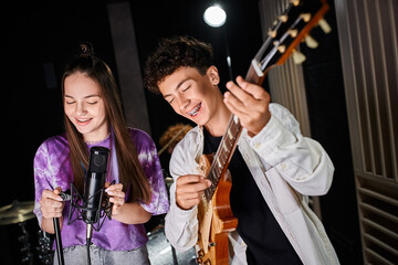 good looking cheerful teenage boy with braces playing guitar next to his cute vocalist in studio