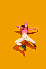 Fototapeta na wymiar Dynamic full length portrait of attractive young girl, dressed fashion outfit jumping and posing in motion against vivid yellow background. Concept of beauty, modern style, shopping, sales. Ad