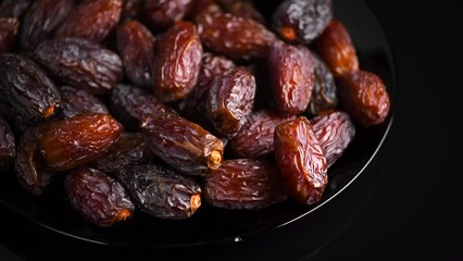 Dates fruit. Date fruits rotating on black background. Big plate full of Medjool dates close up. Tasty healthy Food