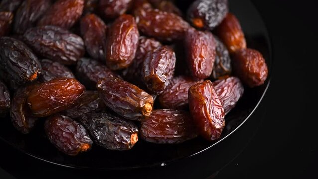 Dates fruit. Date fruits rotating on black background. Big plate full of Medjool dates close up. Tasty healthy Food