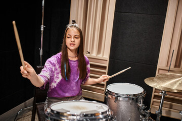 good looking stylish teenage girl in casual vibrant attire playing her drums while in music studio