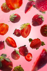 Strawberries and sliced strawberry flying in the air, isolated on pink background.