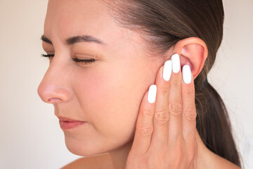 close up photo of young caucasian brunette woman is experiencing acute pain in her ear. She frowns,...