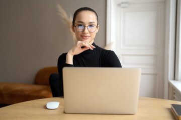 Elegant woman freelancer professional using laptop, confident gaze behind blue light glasses.