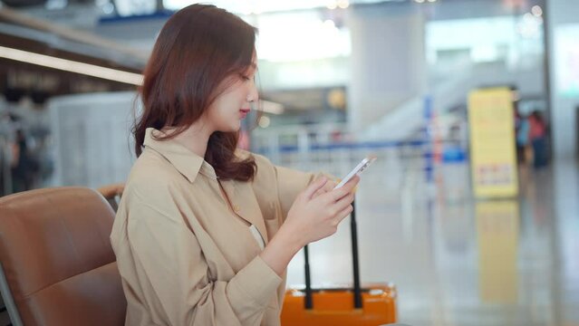 Asian tourist woman using mobile phone and watching watch between waits for flight in Airport Terminal, Browse Internet, Post on Social Media, flight check check in, Tourist journey trip concept