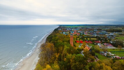 Captured by drone on a cloudy November day, the Gąski lighthouse stands against the somber sky. The tranquil sea with gentle waves laps an empty beach. © Grzegorz
