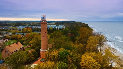 Captured by drone on a cloudy November day, the Gąski lighthouse stands against the somber sky. The tranquil sea with gentle waves laps an empty beach. - Powered by Adobe
