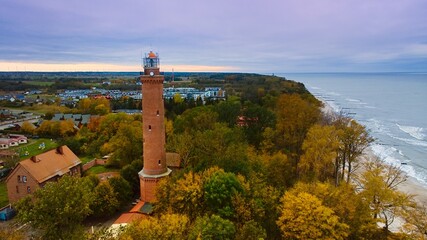 Captured by drone on a cloudy November day, the Gąski lighthouse stands against the somber sky. The tranquil sea with gentle waves laps an empty beach. © Grzegorz