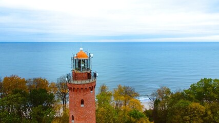 Captured by drone on a cloudy November day, the Gąski lighthouse stands against the somber sky. The tranquil sea with gentle waves laps an empty beach. © Grzegorz