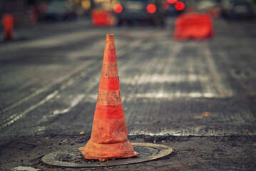 Orange traffic cone stands on manhole. Road repair works, asphalt laying, pylon to mark an obstacle...