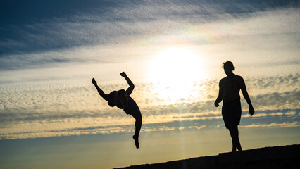 Silhouette of two boys jump from the jetty while sunset