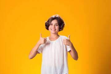 Smiling kid girl showing thumbs up gesture over yellow background. Success concept