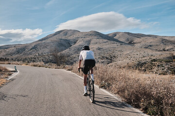 A man is riding a gravel bicycle on the road in the hills with a mountain view. Athlete wearing white and black cycling kit and black helmet on a gravel bike. Cycling adventure in Spain.